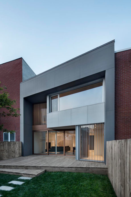 Modern two-story facade with sleek gray panels, wooden deck, and glass entryway.