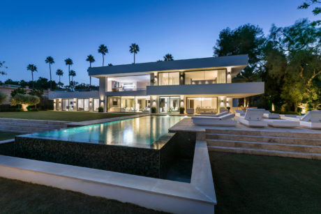 Striking modern villa with expansive glass walls, infinity pool, and lush landscaping.
