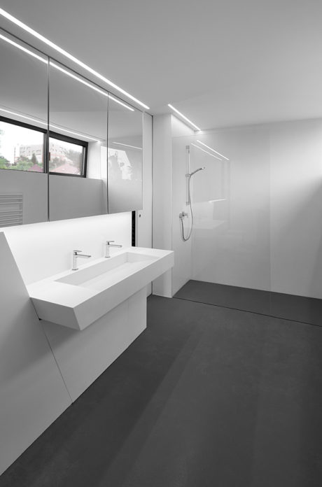 A modern bathroom with minimalist white vanity, glass shower partition, and sleek lighting.