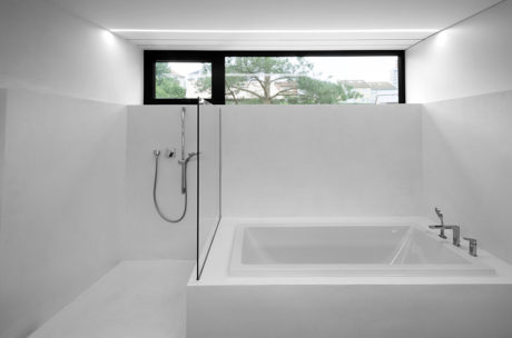 A modern bathroom with a sleek white tub, minimalist fixtures, and a large window overlooking greenery.