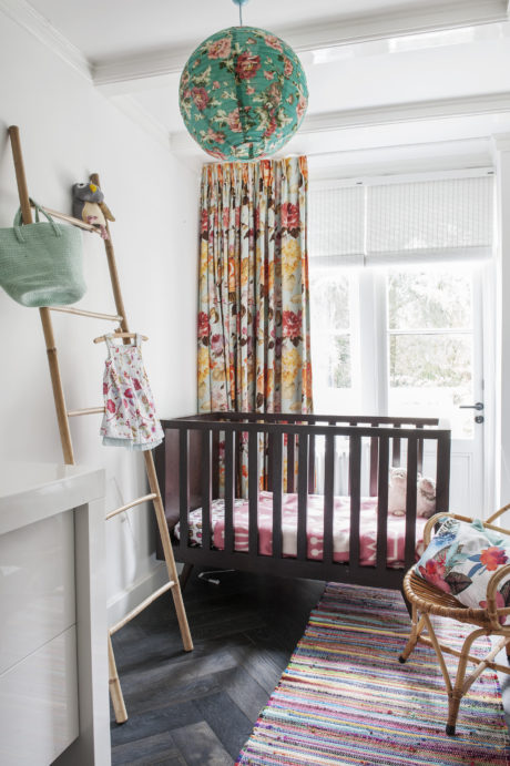 A cozy nursery with a vibrant floral-patterned light fixture, crib, and rug.