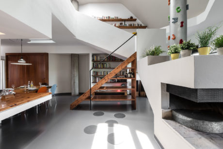 Modernist loft interior with wooden stairs, shelving, and kitchen counter. Accent plants enhance the space.