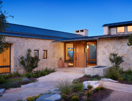 Stone facade house with metal roof and landscaped garden at dusk.