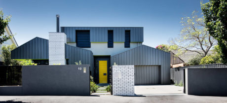 Contemporary residential building with metal and brick facade, yellow door, and garage.
