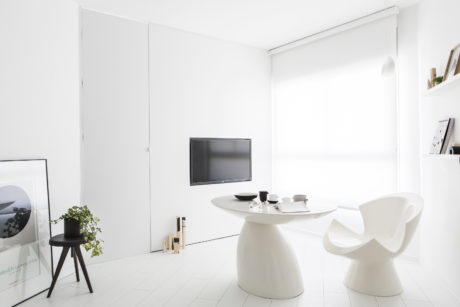 Minimalist white room with curved table, chairs, and wall-mounted TV. Sleek, modern design.