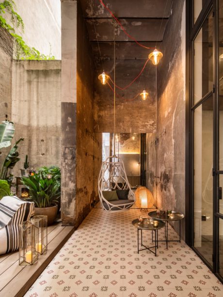 Rustic industrial interior with patterned tile floor, hanging lamps, and cozy furniture.