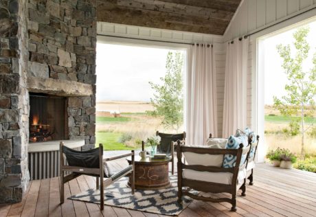 Rustic porch with stone fireplace, wooden floors and countryside view.