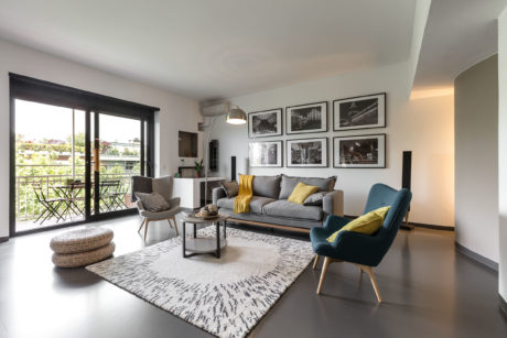 A modern, stylish living room with a gray sofa, vibrant chairs, and framed art on the walls.