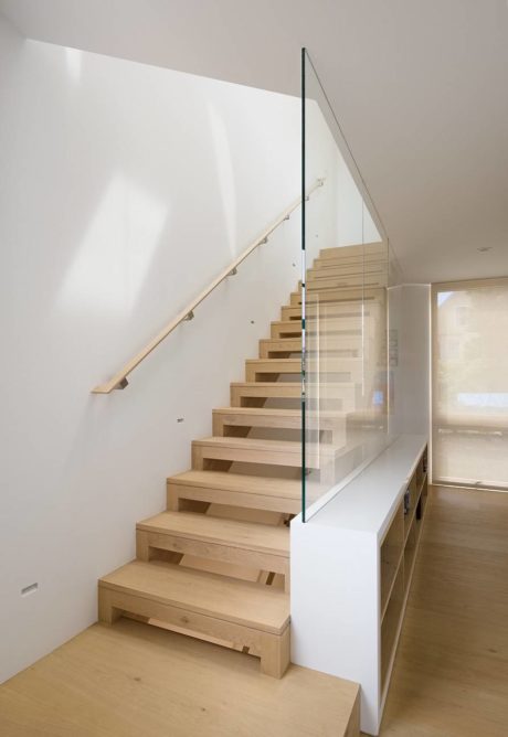 Modern wooden staircase with glass railing in a minimalist interior.