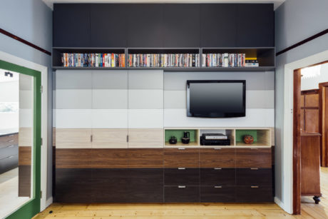 A modern, minimalist living room with a built-in entertainment unit featuring dark cabinets, open shelves, and a mounted TV.