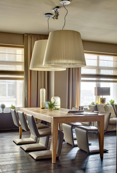 A spacious dining room with a wooden table, plush chairs, and a pair of hanging lamps.