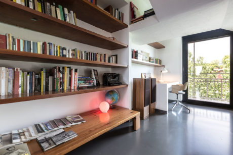 Spacious home study with wooden bookshelves, desk, and large window overlooking greenery.