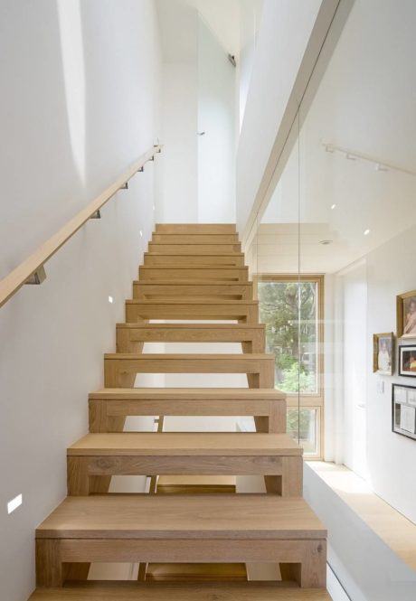 Modern wooden staircase with glass balustrade in a white interior.