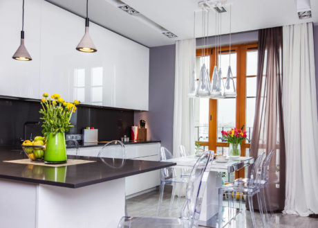 Modern kitchen with sleek black countertop, pendant lights, and transparent chairs.