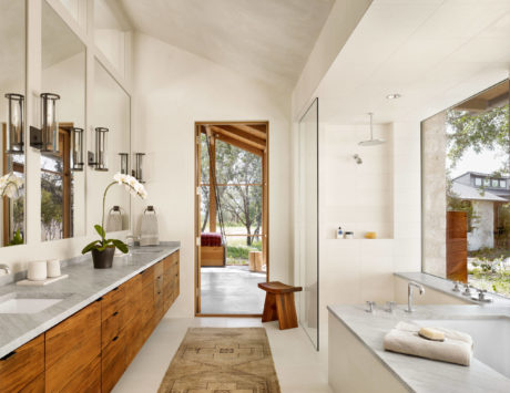 Elegant bathroom with wood cabinetry and marble counters, opening to nature.