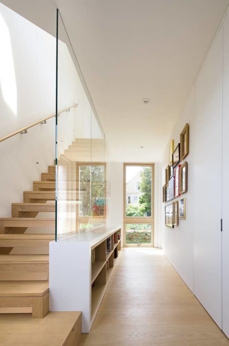 Bright hallway with a wooden staircase and glass balustrade, leading to framed art