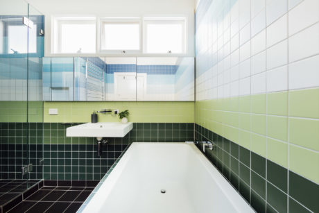 A modern bathroom with contrasting green and black tiles, a large tub, and a vanity sink.