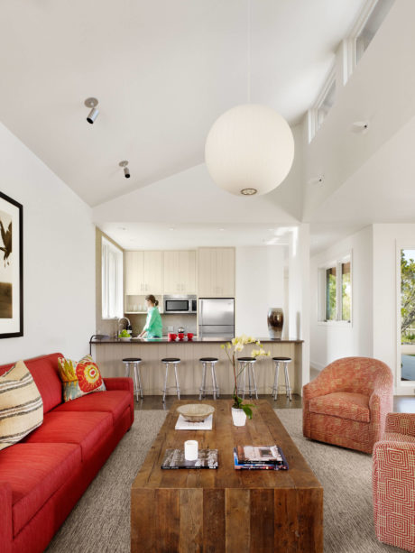 Modern living room with red couch, wooden table, and open kitchen.