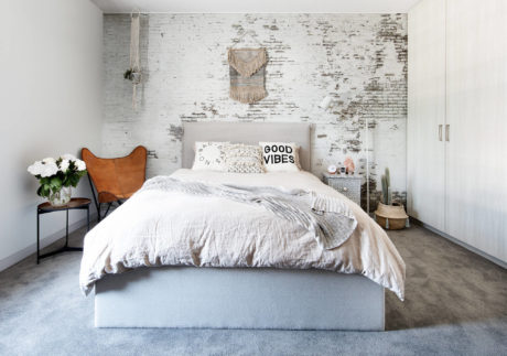 Rustic, modern bedroom with exposed brick wall, macrame decor, and cozy furnishings.