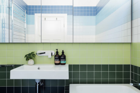 Modern bathroom with contrasting blue and green tiles, sleek white vanity, and natural decor.