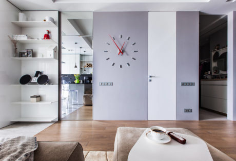 Modern, minimalist living room with sleek built-in shelving, large wall clock, and cozy furnishings.