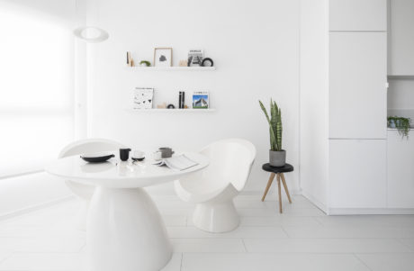 Minimalist dining area with white furniture, shelves, and a potted plant, showcasing clean interior design.