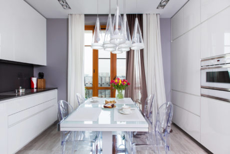 Modern kitchen with sleek white cabinetry, glass dining table, and stylish chandelier.