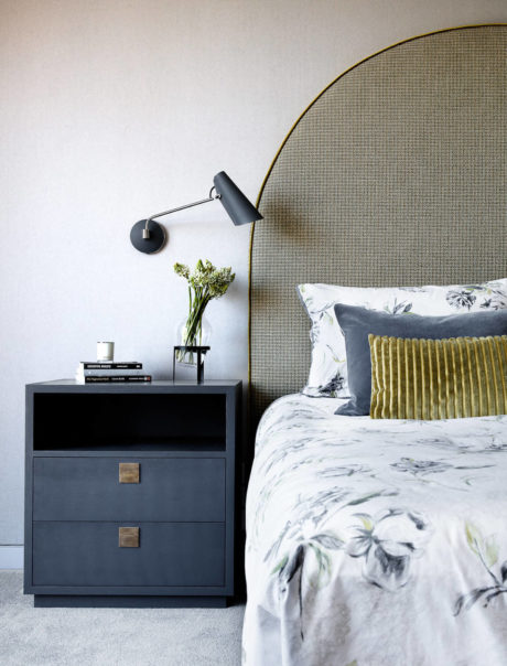 Minimalist bedroom with gray-toned headboard, black nightstand, and wall-mounted lighting.
