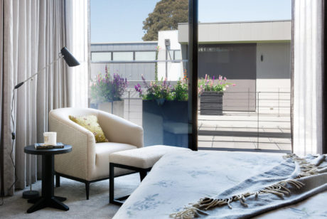Stylish bedroom with a modern armchair, plants, and a view of the outdoor architecture.