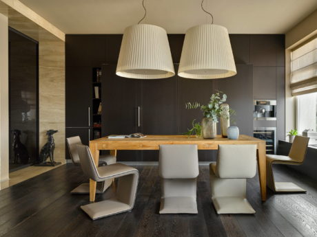 Modern dining room with wooden table, white pendant lamps, and dark cabinetry.