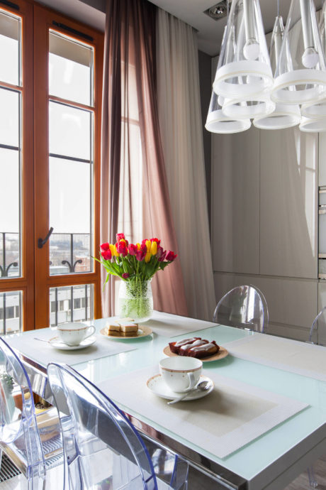 A contemporary dining room with a chandelier, tulip arrangement, and glass table.
