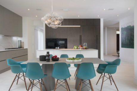 Modern kitchen and dining area with sleek cabinetry, table, and turquoise chairs.