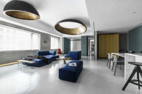 Sleek, modern living space with bold blue sofas, gold-accented ceiling lights, and marble surfaces.