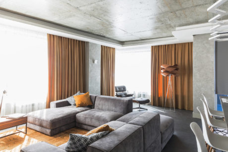 Spacious room with concrete ceiling, large gray sectional sofa, and floor-to-ceiling curtains.