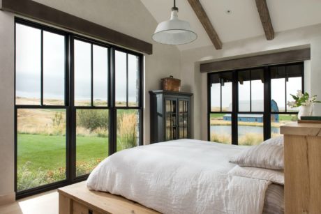 Rustic-chic bedroom with large windows and exposed beams, overlooking serene landscape