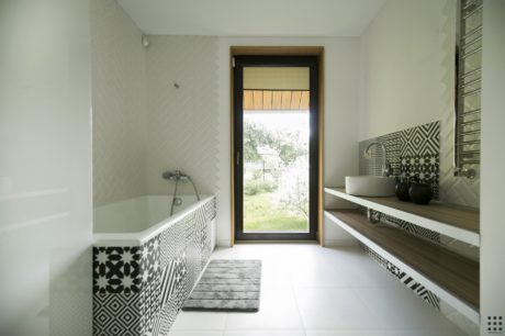 Elegant bathroom with geometric tile patterns, wooden vanity, and large window overlooking nature.