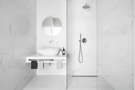 Modern minimalist bathroom with sleek white vanity, round mirror, and rainfall shower.