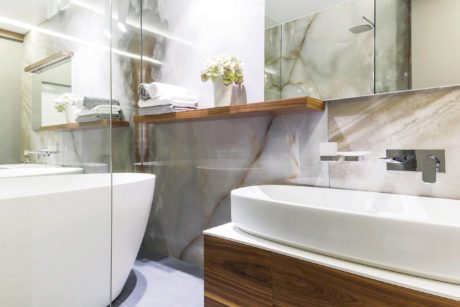 A modern bathroom featuring a wooden vanity, large mirror, and marble tile walls.
