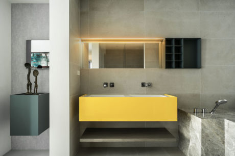 Sleek modern bathroom with yellow vanity, gray tile walls, and sculpted decor accents.