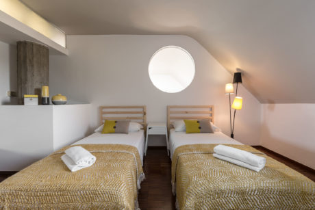 A cozy, well-lit bedroom with matching twin beds, wooden headboards, and circular window.