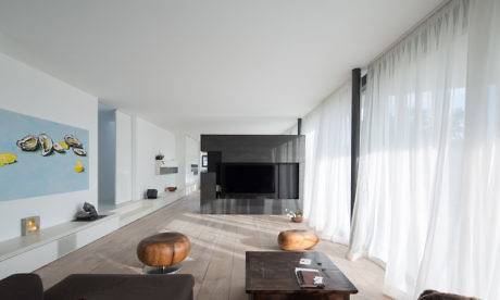 Modern living room with white walls, sheer curtains, and dark furniture.