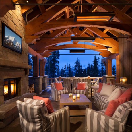 Cozy wooden outdoor patio with fireplace and striped furniture at dusk.