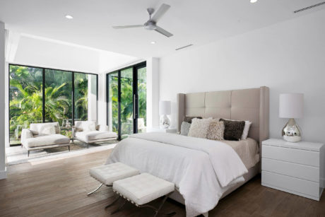 Modern bedroom with large bed, white decor, and floor-to-ceiling windows.