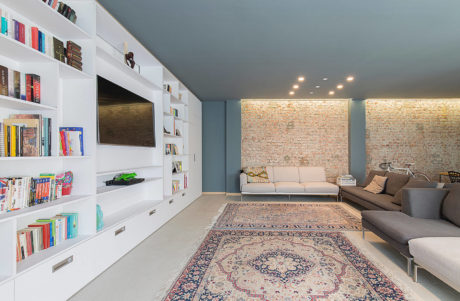 Modern living room with white shelving, exposed brick wall, and Persian rug.