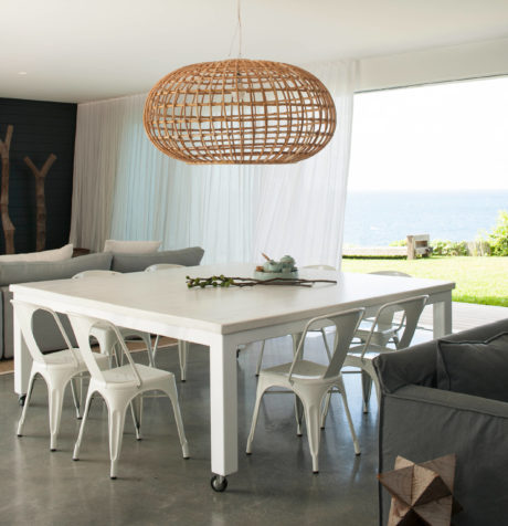 Modern dining room with a large wicker pendant light, white table, and ocean