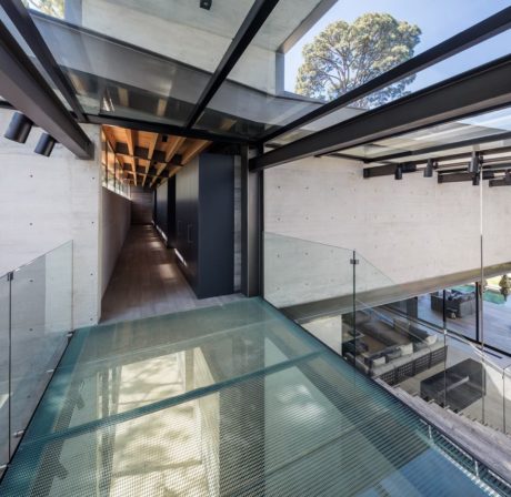 Modern corridor with glass floor and wood ceiling, surrounded by concrete walls.