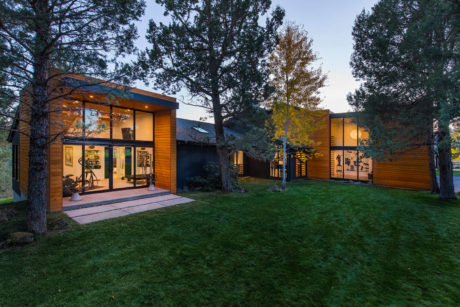 Contemporary home with ample glazing, nestled among trees at dusk.