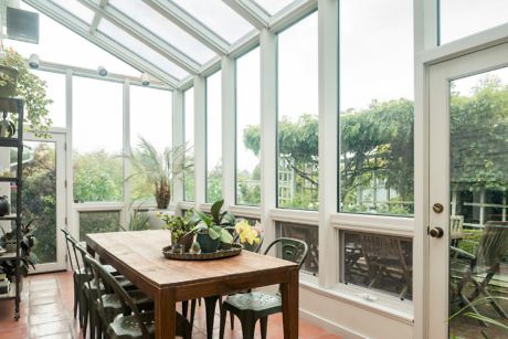 Sunlit conservatory with glass ceiling and wooden dining set.