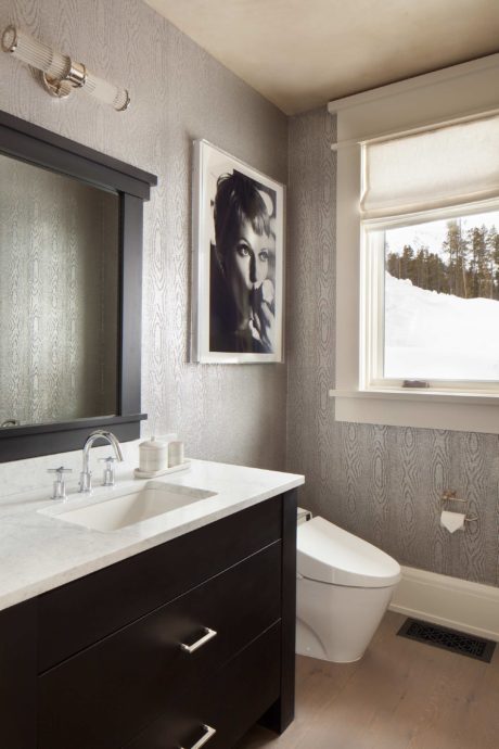 Modern bathroom with dark vanity, framed portrait, and snowy view outside.