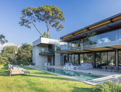 Modern house with large glass windows, pool, and verdant garden.